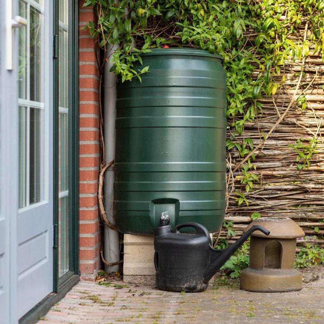 Green water butt in a garden with a watering can next to it