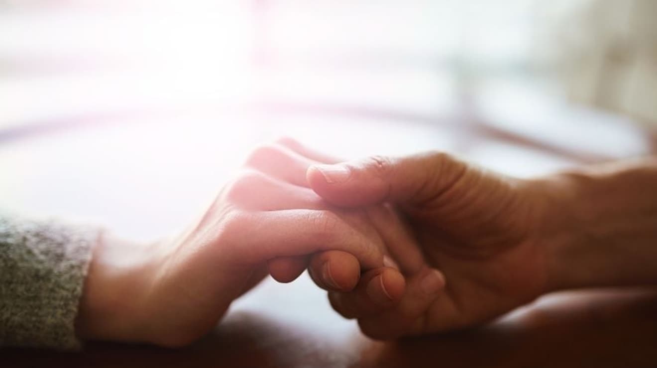 Hands holding across a table against a blurred background