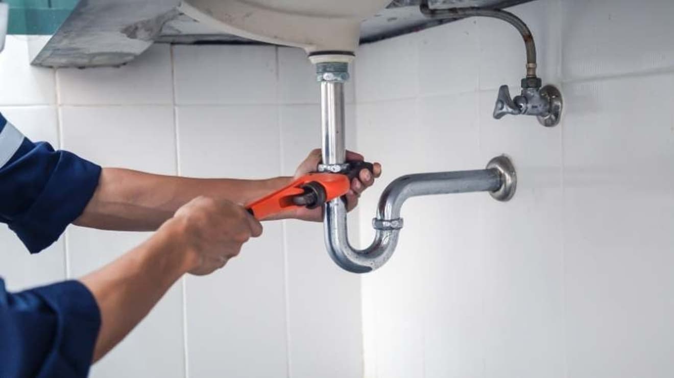 plumber crouching down under the sink to get to the pipework