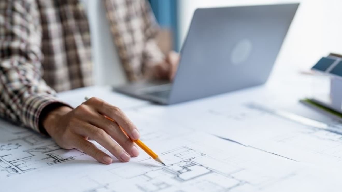 man looking at development plans on a table whilst working on a laptop