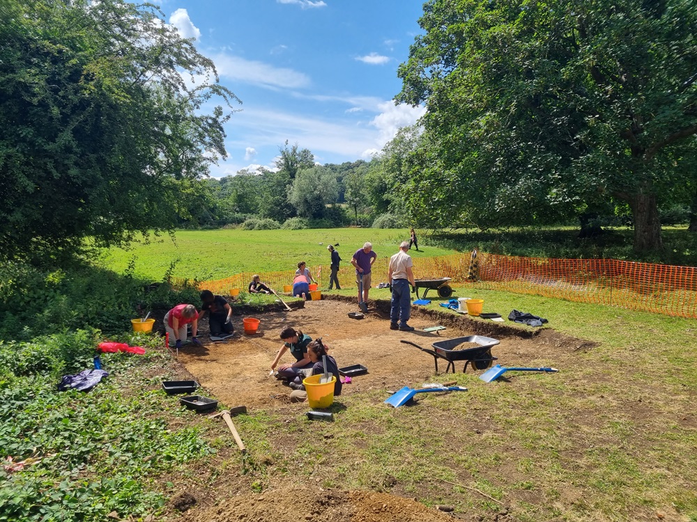 Team of people on sunny day, excavating ground area with wheel barrows and tools for digging